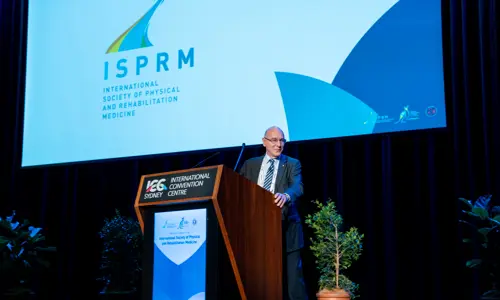 ISPRM World Congress speaker on stage addressing audience with presentation in background