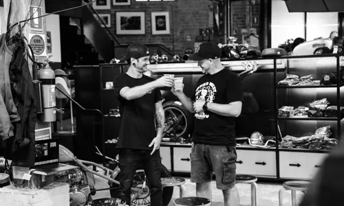 Two guests cheering with beer in hand amongst motorbike merchandise at Young Henrys