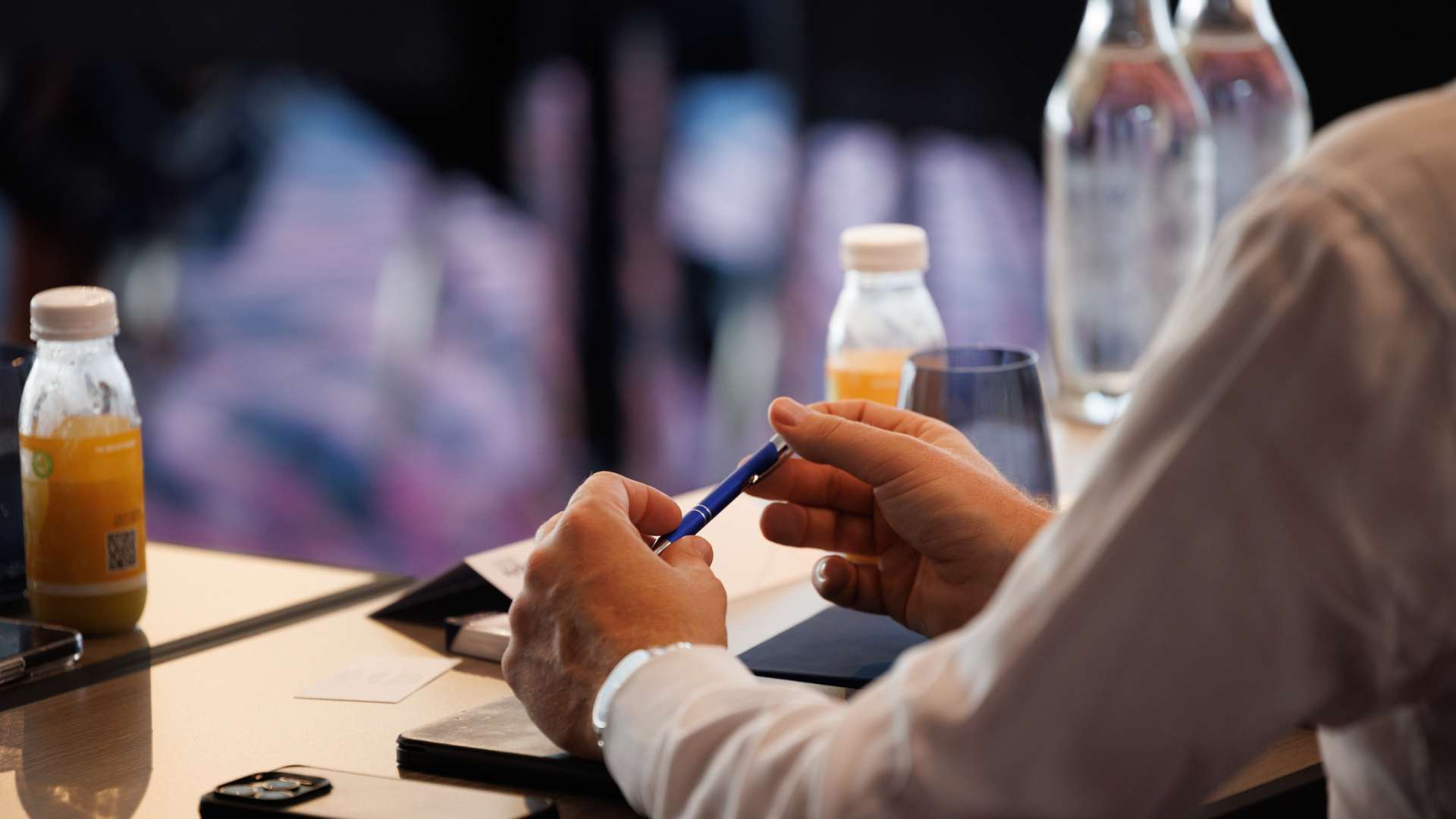 A man at a conference showing his hands on the table holding a pen 