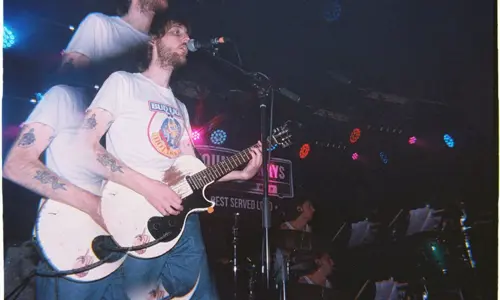 Musician playing guitar with band on stage at Young Henrys