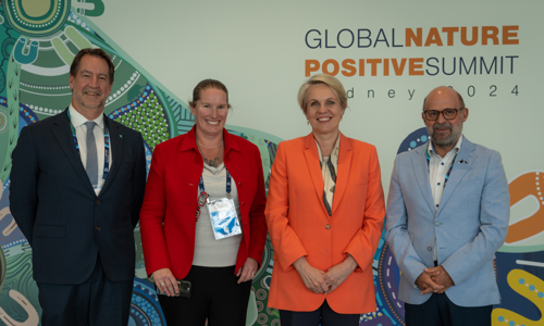 Four Conference Attendees Standing In Front Of Large Entrance Board With The Title Name Of Conference Global Nature Positive Summit Logo