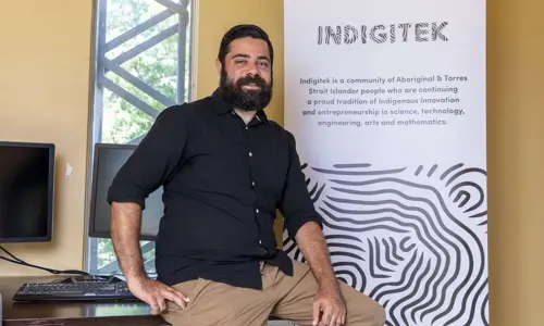 Liam Ridgeway, Co-Founder at Indigitek, posing in front of an Indigitek banner