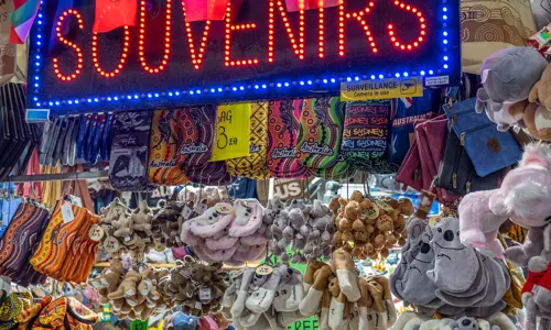 Stuffed toys, keyrings, pouches and more hand below a neon souvenirs sign at a market