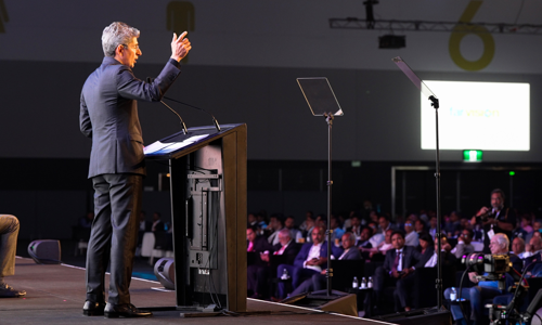Side profile view of speaker on stage addressing conference delegates